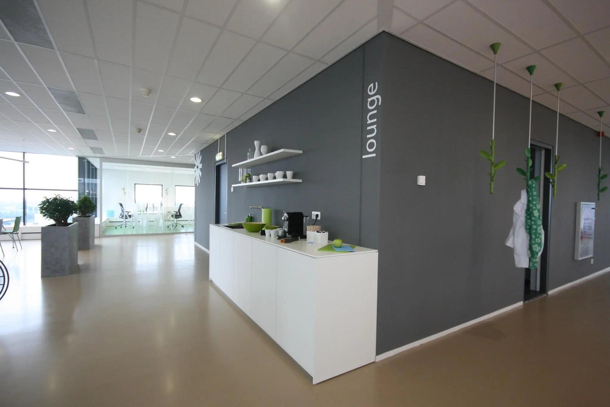 Moderne loungehoek in een kantoorpand in Rivium Quadrant met koffiecorner en uitzicht op vergaderruimte.